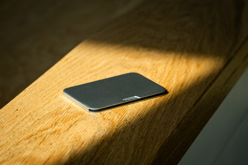 A silver aluminium Ohsnap Wallet 2 on a sunlit wooden surface, its thin edge profile catching the light.