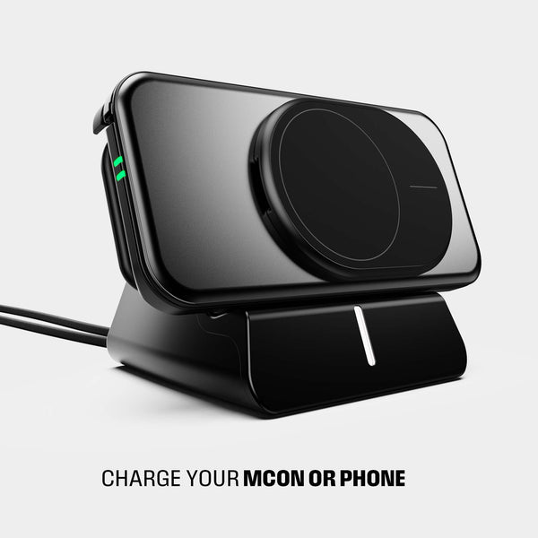 Black charging dock with a phone placed on it, featuring a green indicator light and a connected cable.