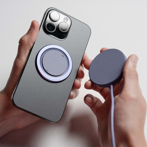 A hand holds a smartphone with a magnetic charging pad attached, while another hand holds a separate magnetic charger.