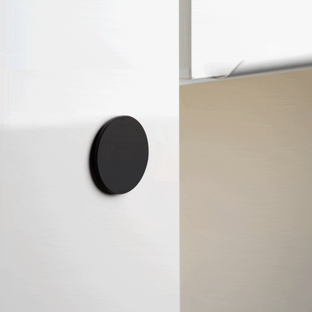 Round black wall mount attached to a white surface, demonstrating its functionality.