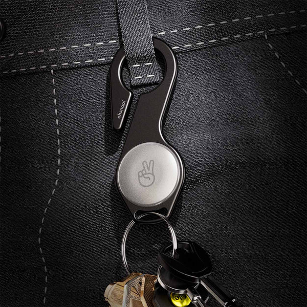 A black key loop attached to a belt loop, holding several keys and featuring a circular button with a peace sign.