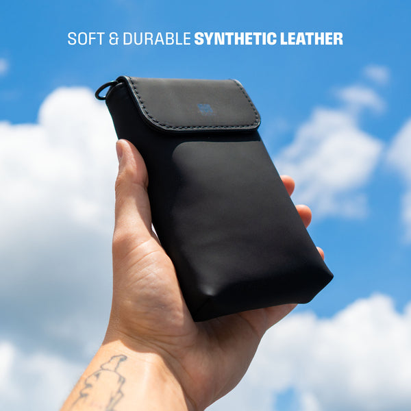 Black synthetic leather travel sleeve held in a hand against a blue sky with clouds.