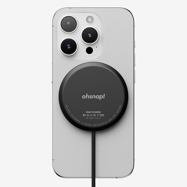 Black wireless charger attached to a smartphone with three rear cameras and a charging cable.