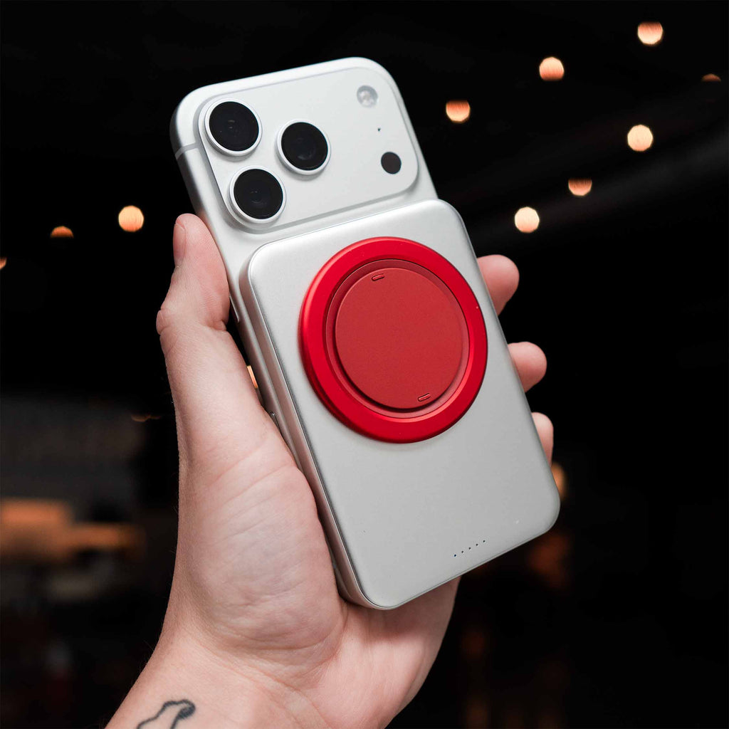 A hand holds a silver phone with a red magnetic accessory attached to the back.
