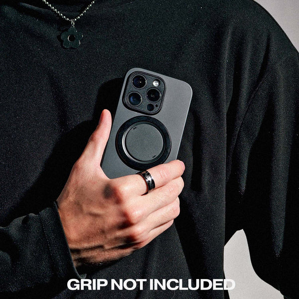 A person holds a gray phone case with a circular attachment, wearing a black shirt and ring.