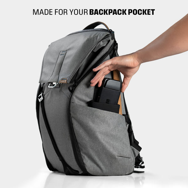 A hand is placing a device into the side pocket of a gray backpack.