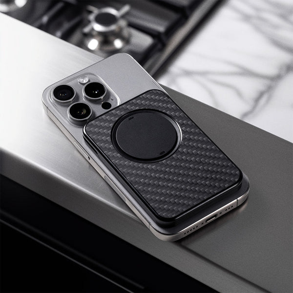 A smartphone with a black Snap Grip Wallet attached, resting on a stainless steel surface.