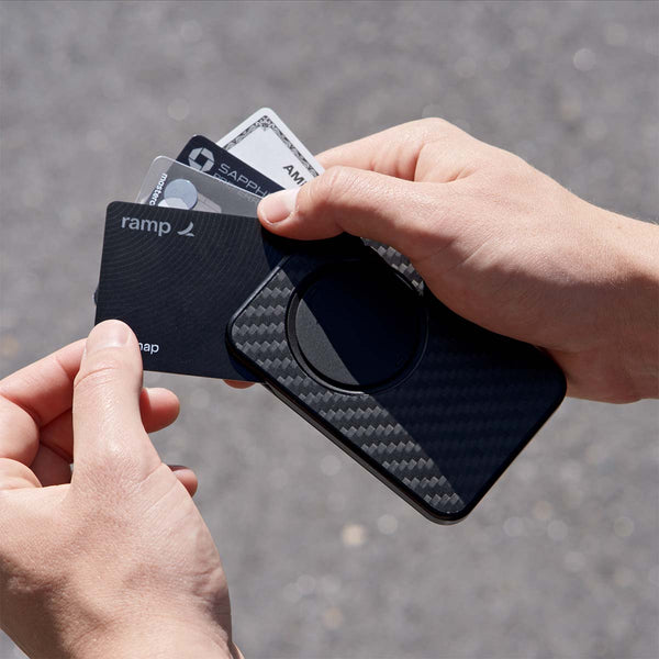 A hand holds a black wallet with a textured surface and several visible credit cards.