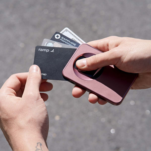 A hand holds a Snap Grip Wallet with several cards partially pulled out against a blurred outdoor background.