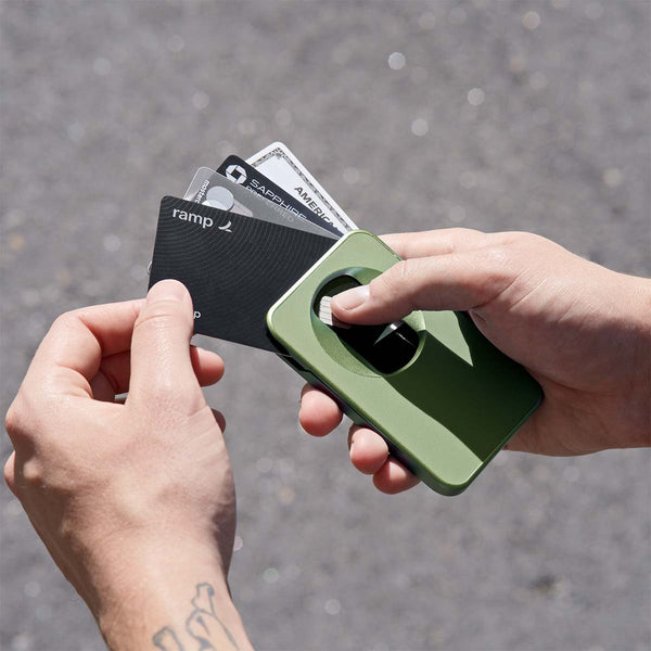 Hands holding a green wallet with several cards partially pulled out, set against a blurred outdoor background.