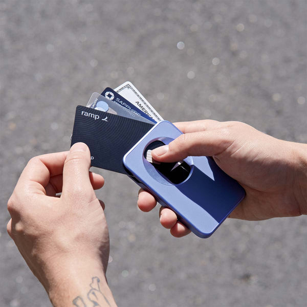 A hand holds a blue wallet with several cards partially pulled out against a blurred outdoor background.