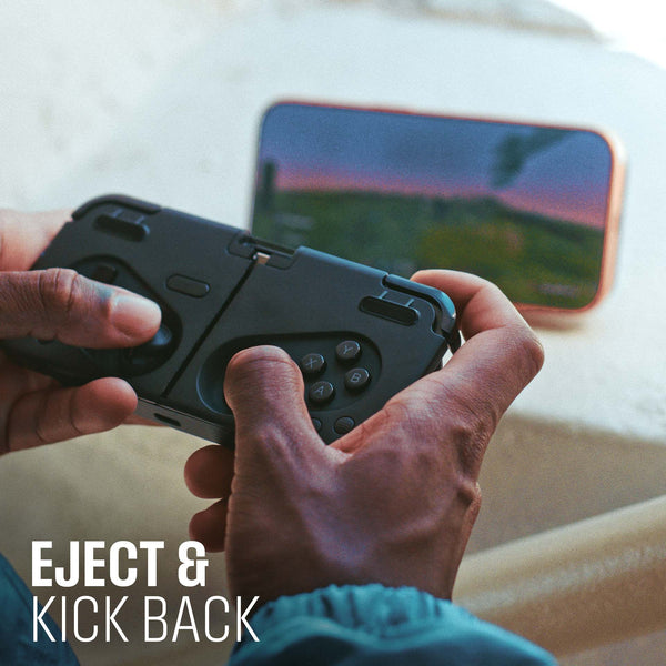 Hands holding a black gaming controller with a smartphone displaying a game in the background.