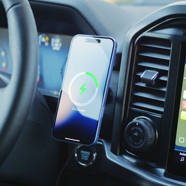 Smartphone charging on a mount in a car, displaying a battery charge status of 21%.