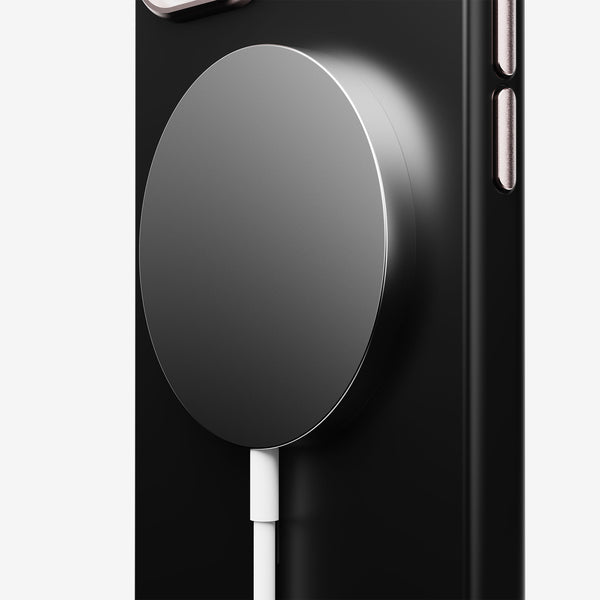 Magnetic charging pad attached to a black phone case, with a white charging cable connected.