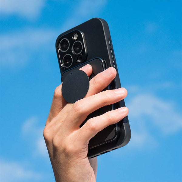 Hand holding a smartphone with a black grip attached, against a blue sky background.