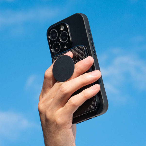 Hand holding a smartphone with a black circular grip against a blue sky.