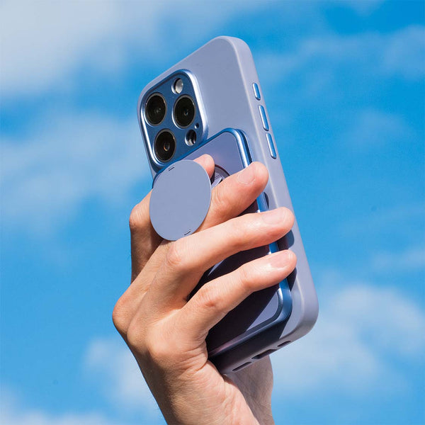 Hand holding a smartphone with a circular grip attached, against a blue sky background.