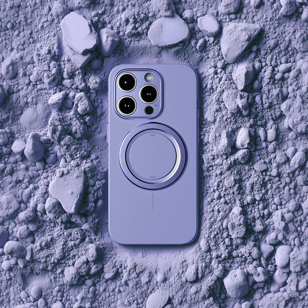 Purple phone case with a circular magnetic attachment, placed on a textured surface of light-colored dust and stones.