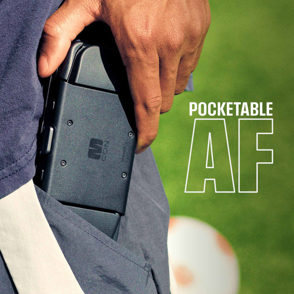 A hand holds a black device partially tucked into a pocket, with grass and a soccer ball visible in the background.