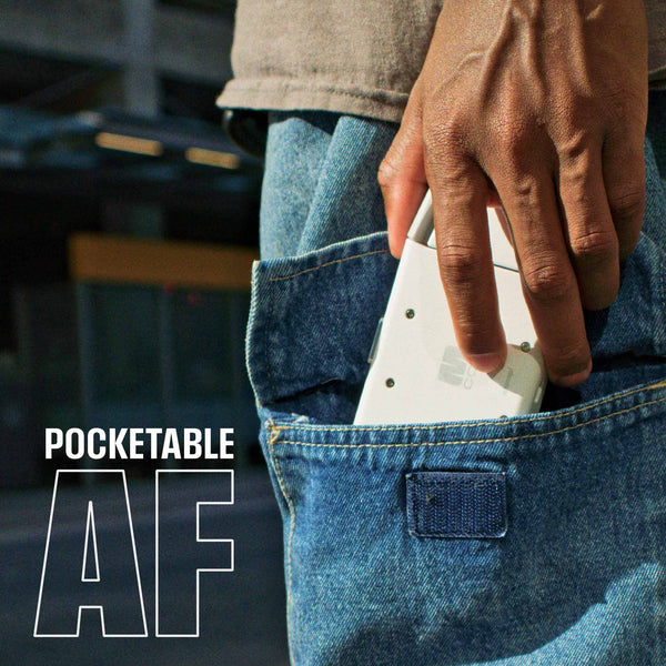 A hand is placing a small white device into the back pocket of blue denim jeans.
