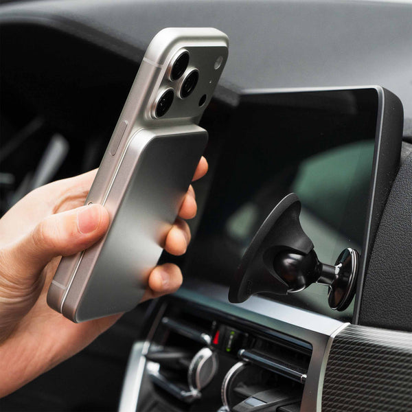 Hand holding a smartphone with a magnetic attachment near a car dashboard mount.
