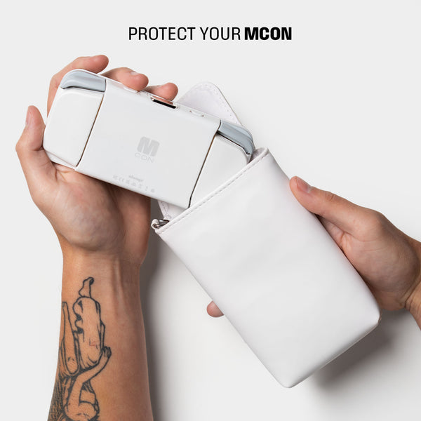 A hand holds a white travel sleeve with an MCON device partially inserted.